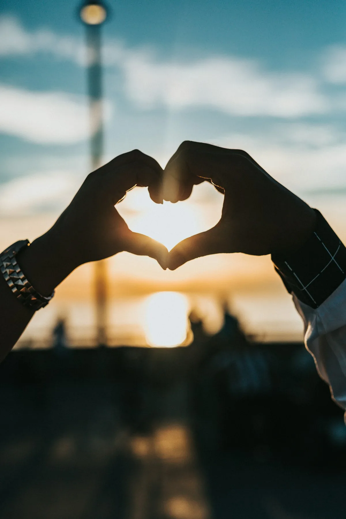 Two hands making a heart shape against a sunset